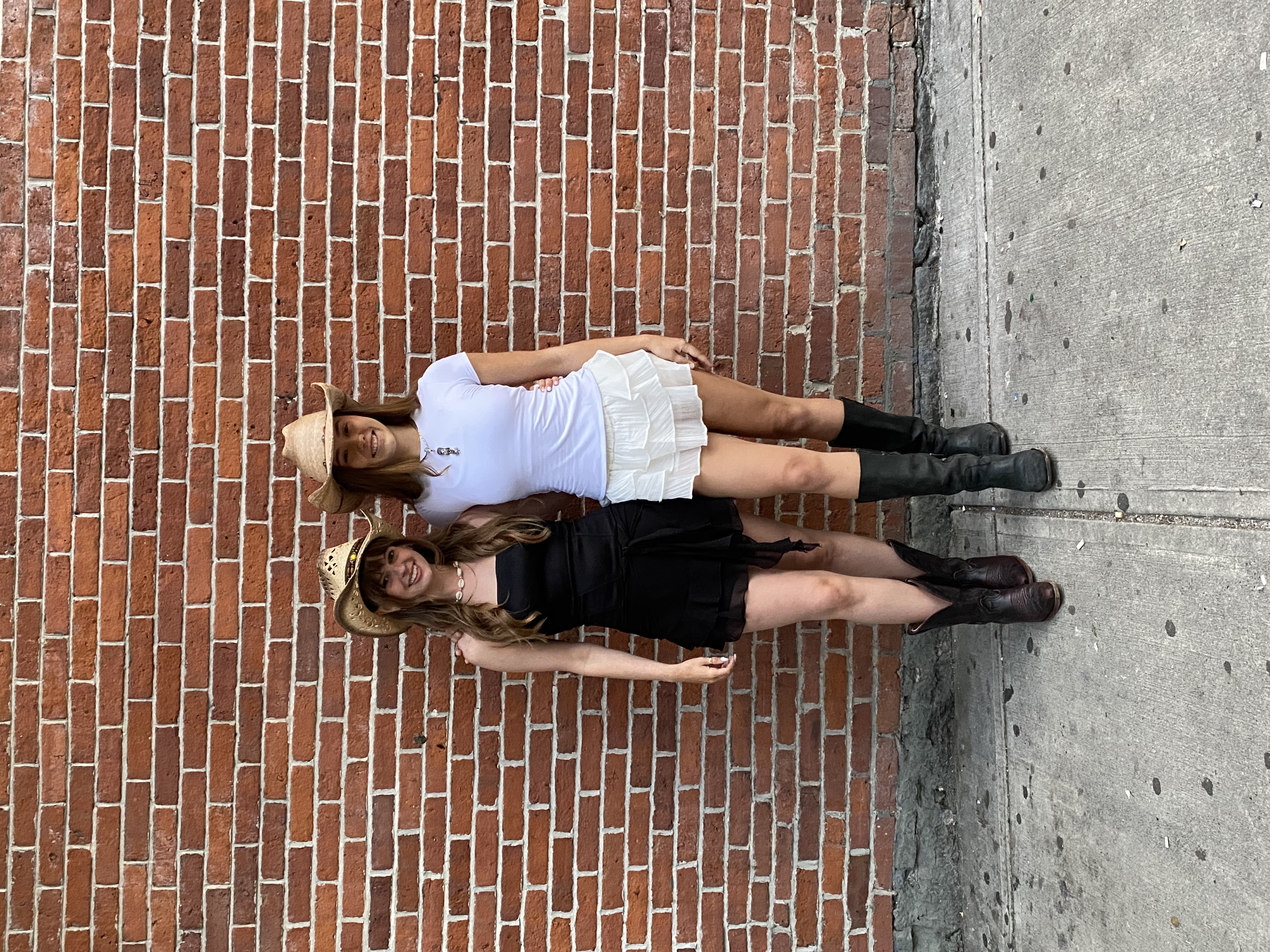 Alex and Lily of Wildflower Line Dancing in cowboy hats and boots smiling in front of a brick wall